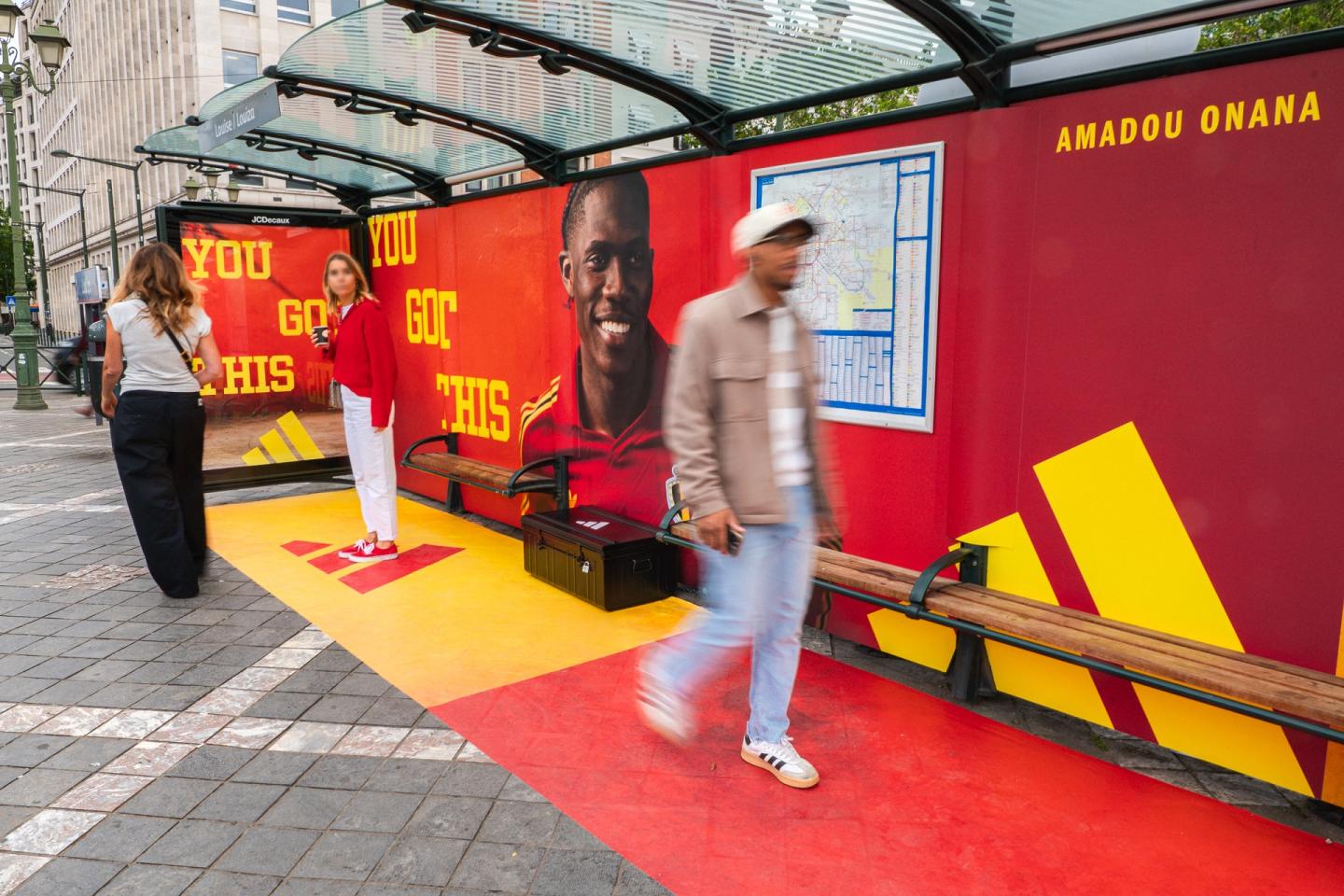 Une mise en scène expérientielle d’un abribus (OOH) issu de l’offre Street de JCDecaux Belgium dans la Brand Zone Louise à Bruxelles met en avant la campagne Bayard Legends d’Adidas. La structure rouge et jaune, avec le portrait d’Amadou Onana et le slogan « YOU GOT THIS », est accompagnée d’un marquage au sol immersif le long duquel les passants circulent.