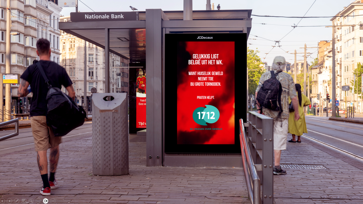 JCDecaux Belgium déploie une campagne programmatic DOOH sur un abribus à Anvers, dans l’univers Digital Street. Ce visuel rouge intense met en avant le slogan alertant sur la hausse des violences domestiques pendant les grands tournois, le numéro 1712 et une ambiance urbaine animée par le passage de piétons.