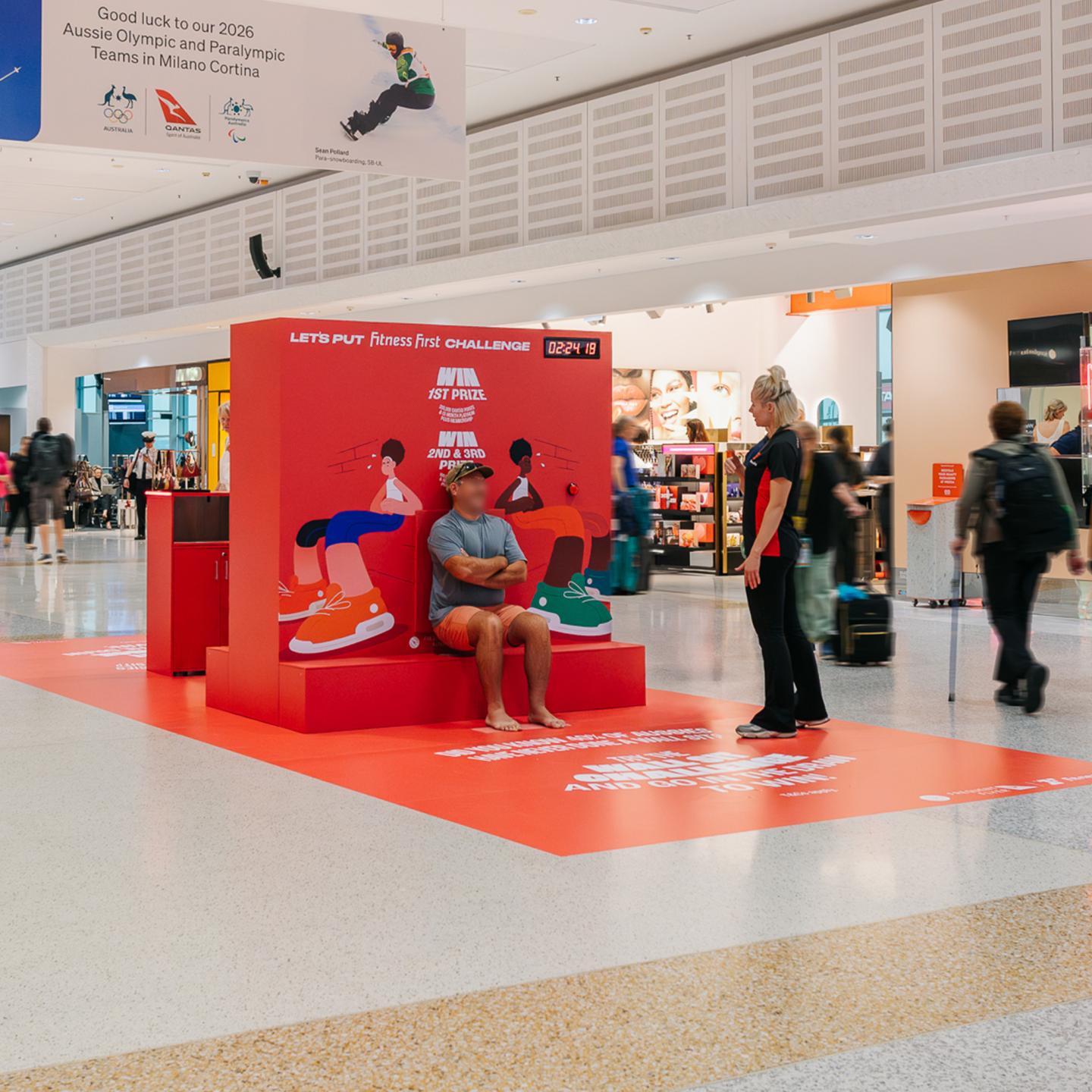 Close-up of the Let’s Put Fitness First interactive wall featuring illustrated characters, campaign messaging and a QR code promoting Qantas Points for new Fitness First members.