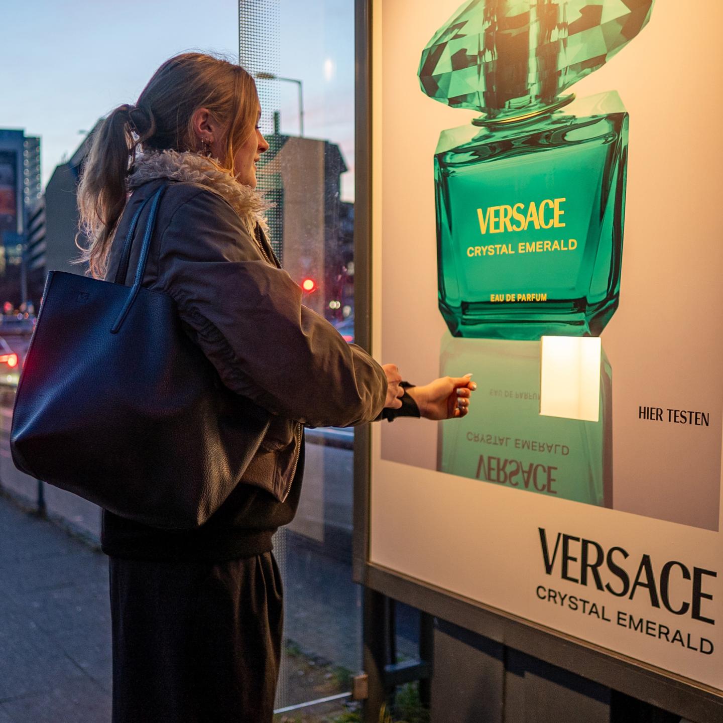 Versace Crystal Emerald olfactory out‑of‑home campaign on a WallDecaux bus shelter, combining striking visuals with a scent diffuser.