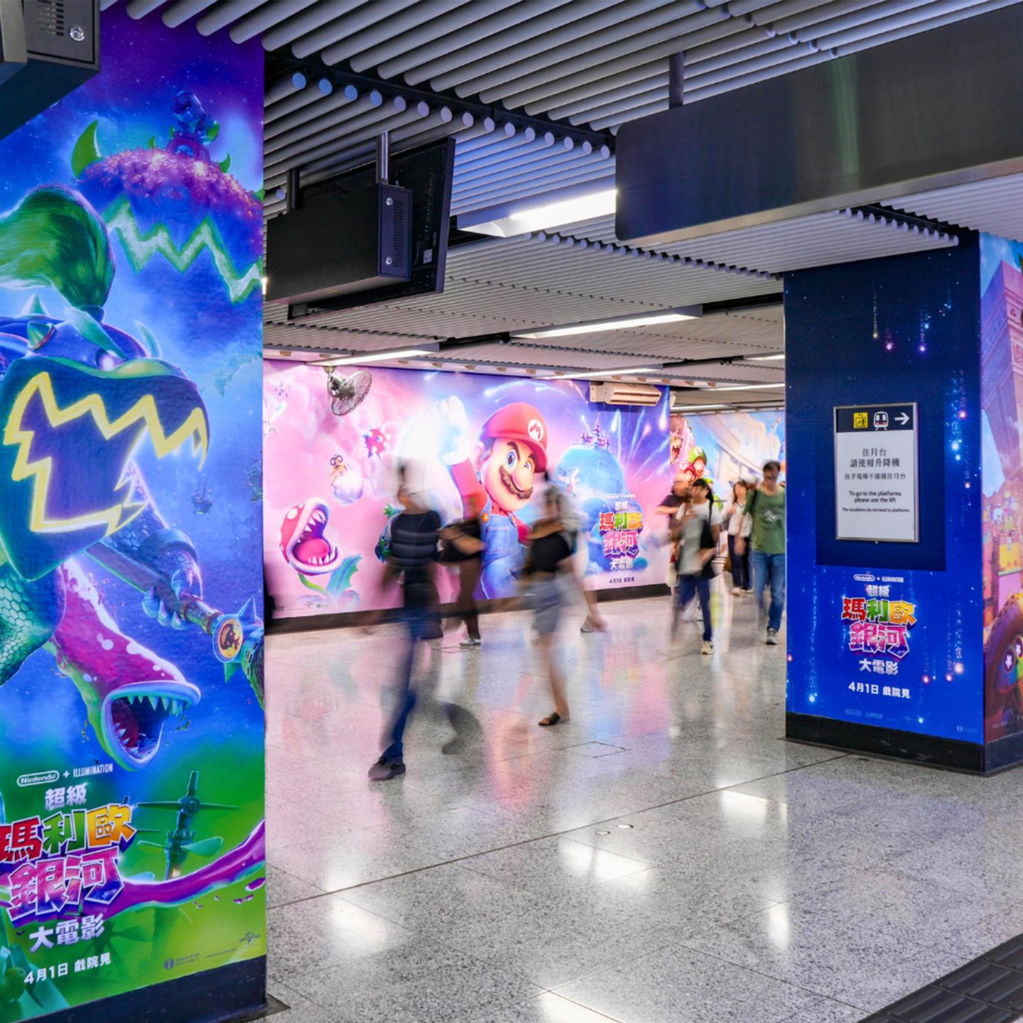 A full station wrap by JCDecaux Transport in Hong Kong, featuring vibrant Super Mario Galaxy graphics on columns and walls throughout the pedestrian walkway
