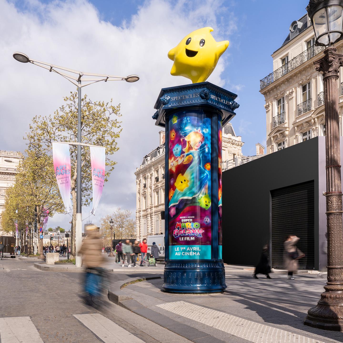 A classic JCDecaux Morris Column on the Champs-Élysées in Paris, topped with a 3D yellow Luma star for the Super Mario Galaxy film campaign