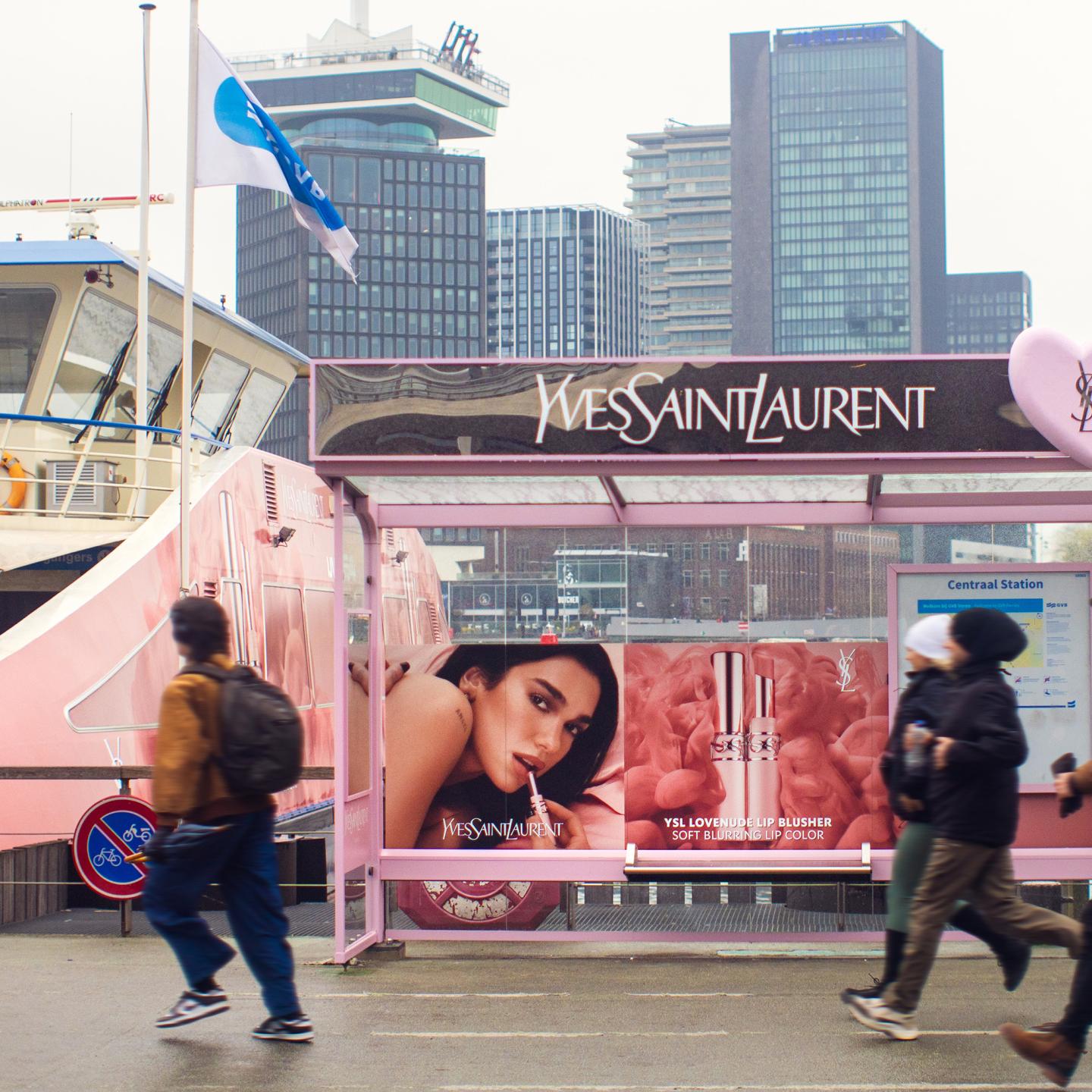 A passenger ferry fully wrapped in pink Yves Saint Laurent Lovenude branding with Dua Lipa, sailing on the Amsterdam canals