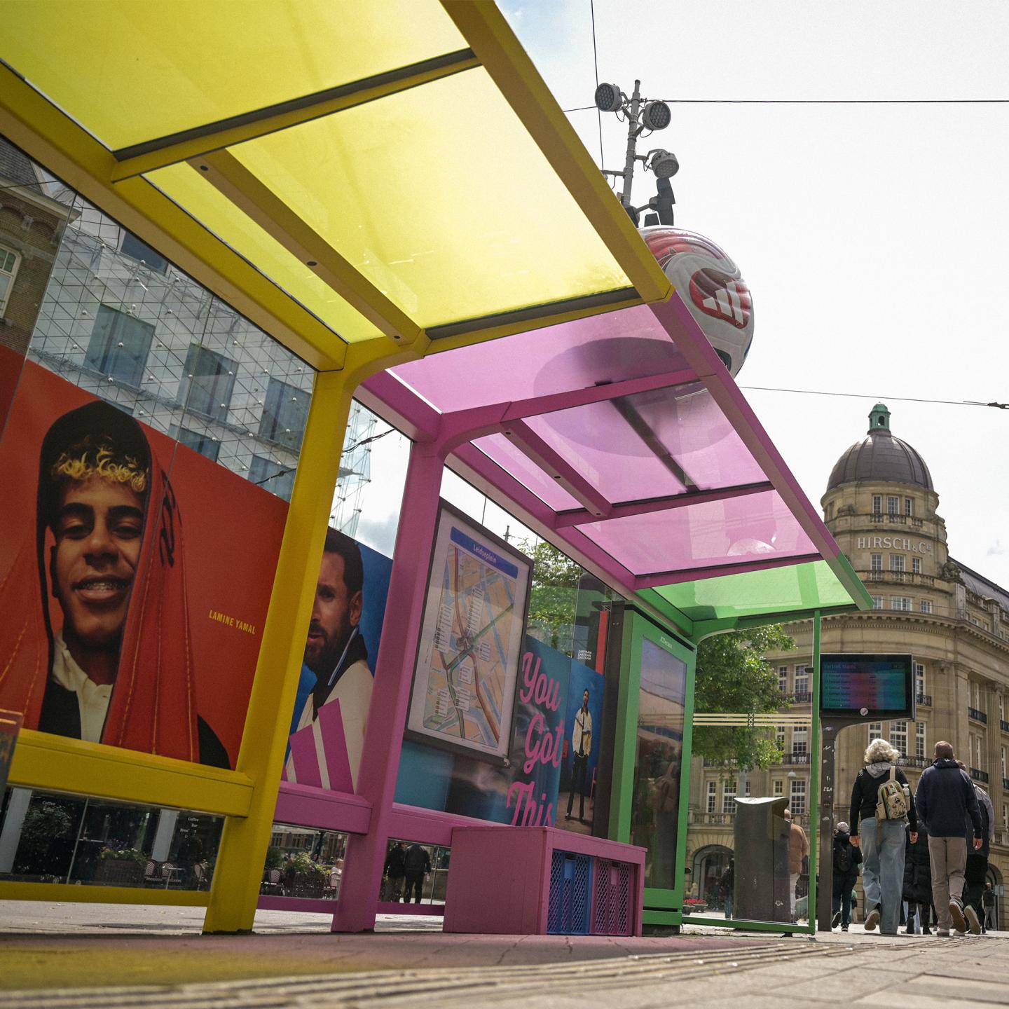 Side view of a JCDecaux bus stop in Amsterdam decorated with adidas World Cup branding and a 3D football on top of the shelter.