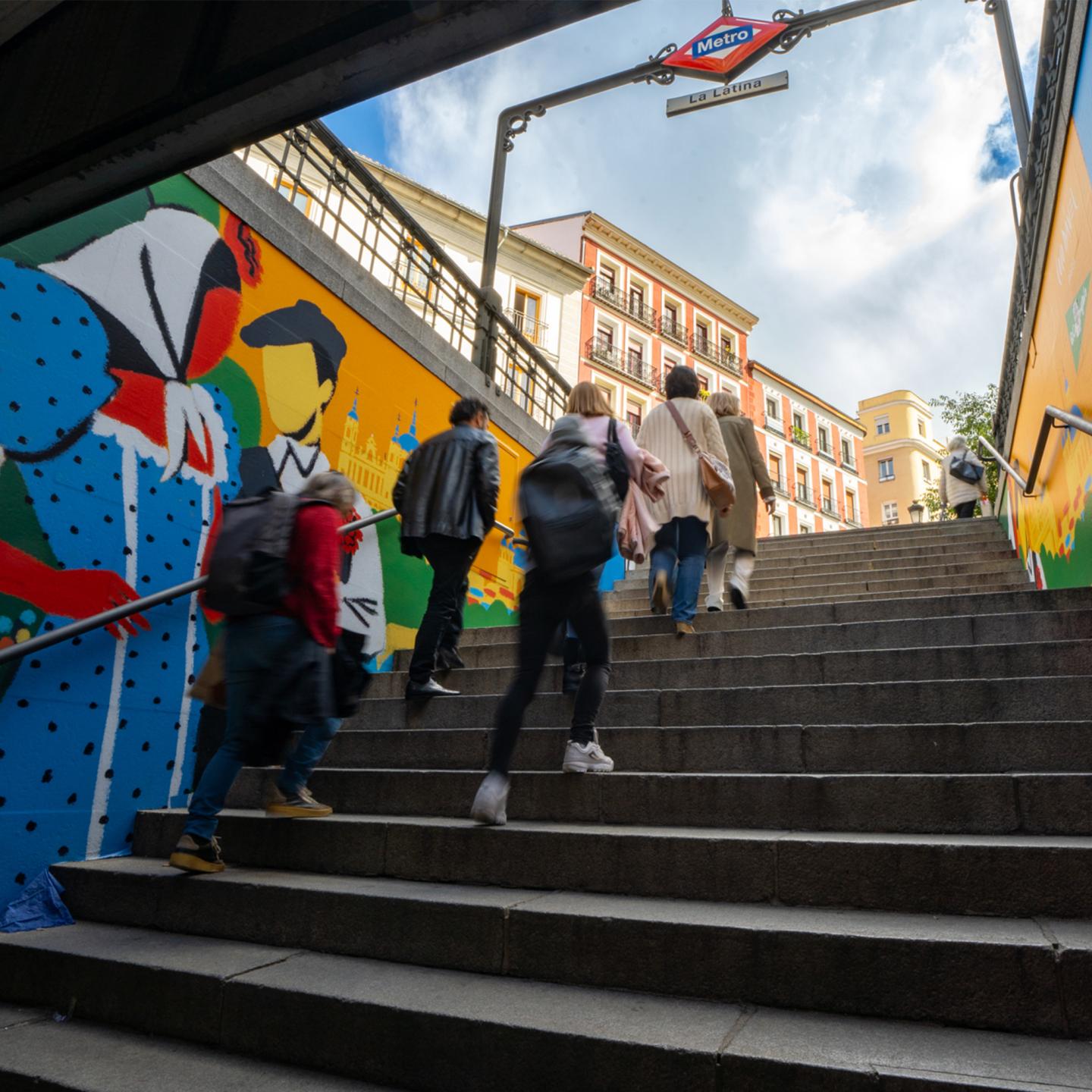 Close-up of a colourful JCDecaux mural by Coco Dávez showing a stylised traditional Madrid couple on the staircase wall of La Latina metro station.