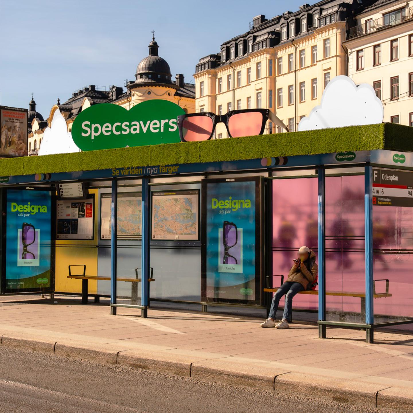 Ultra-colourful JCDecaux bus shelter in central Stockholm featuring Specsavers immersive eyewear campaign with tinted windows, giant glasses on the roof and passers-by enjoying the installation.