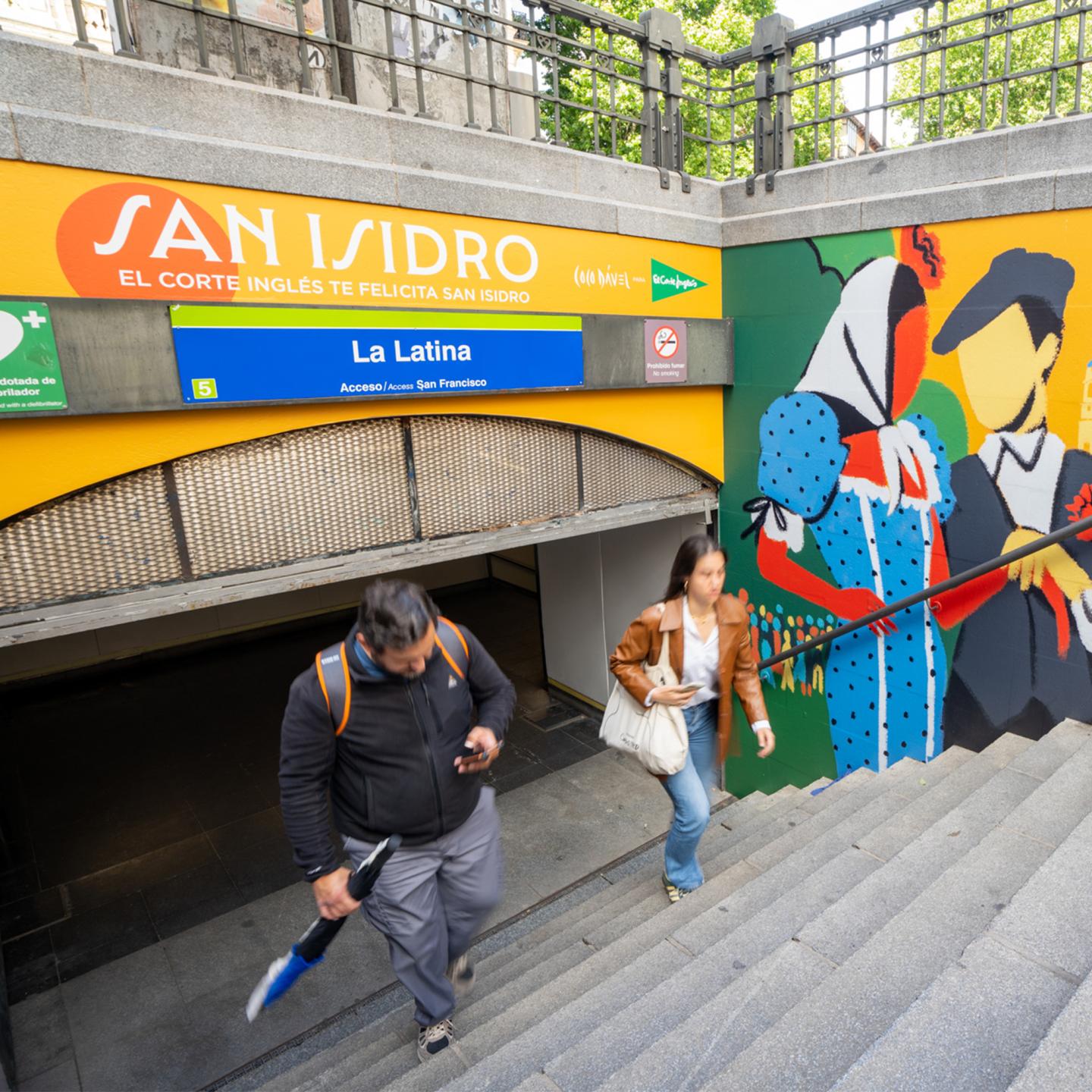 “Group of commuters walking up the stairs next to a large JCDecaux San Isidro mural by Coco Dávez at La Latina metro station in Madrid.