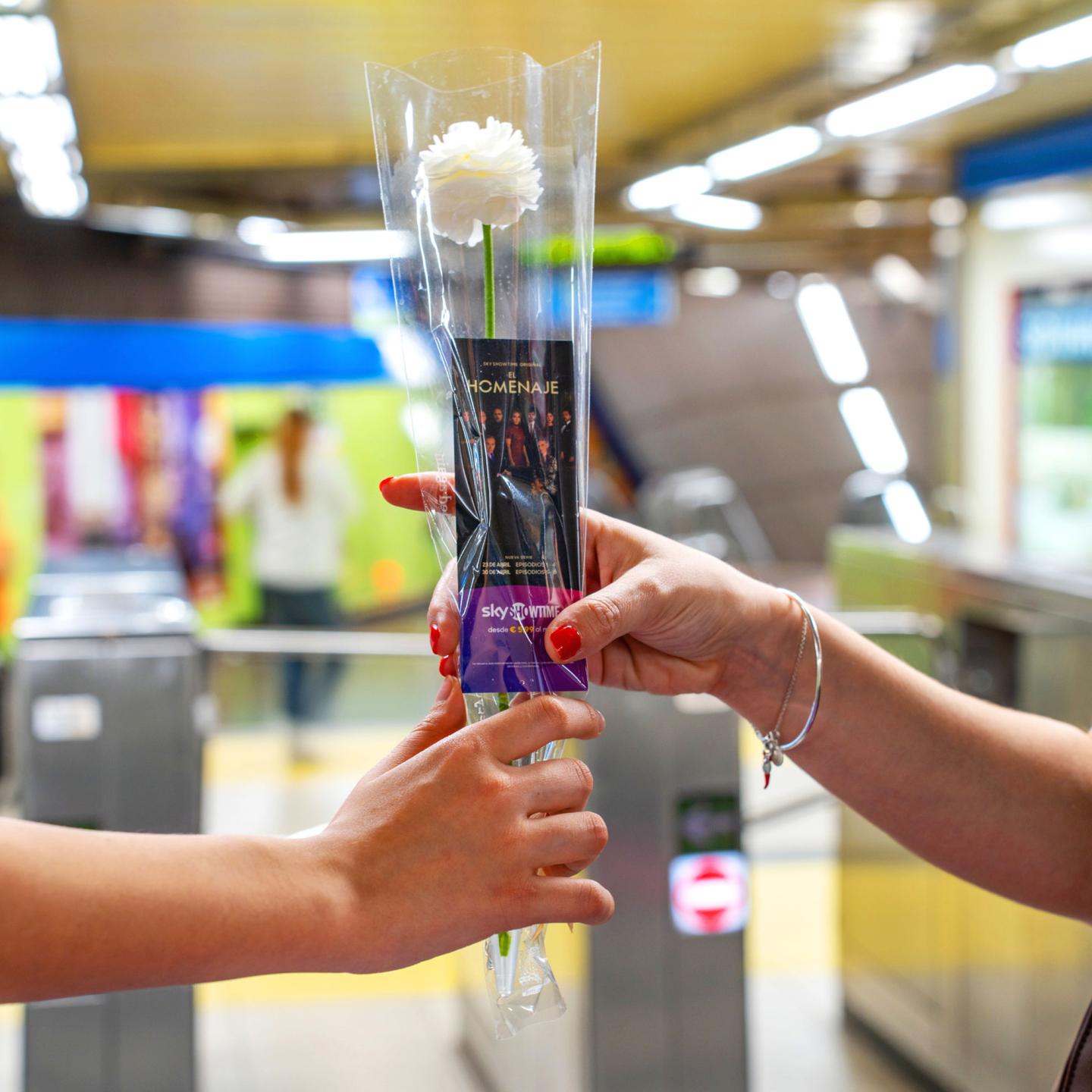 Hand holding a bespoke SkyShowtime bookmark and a fresh white flower.