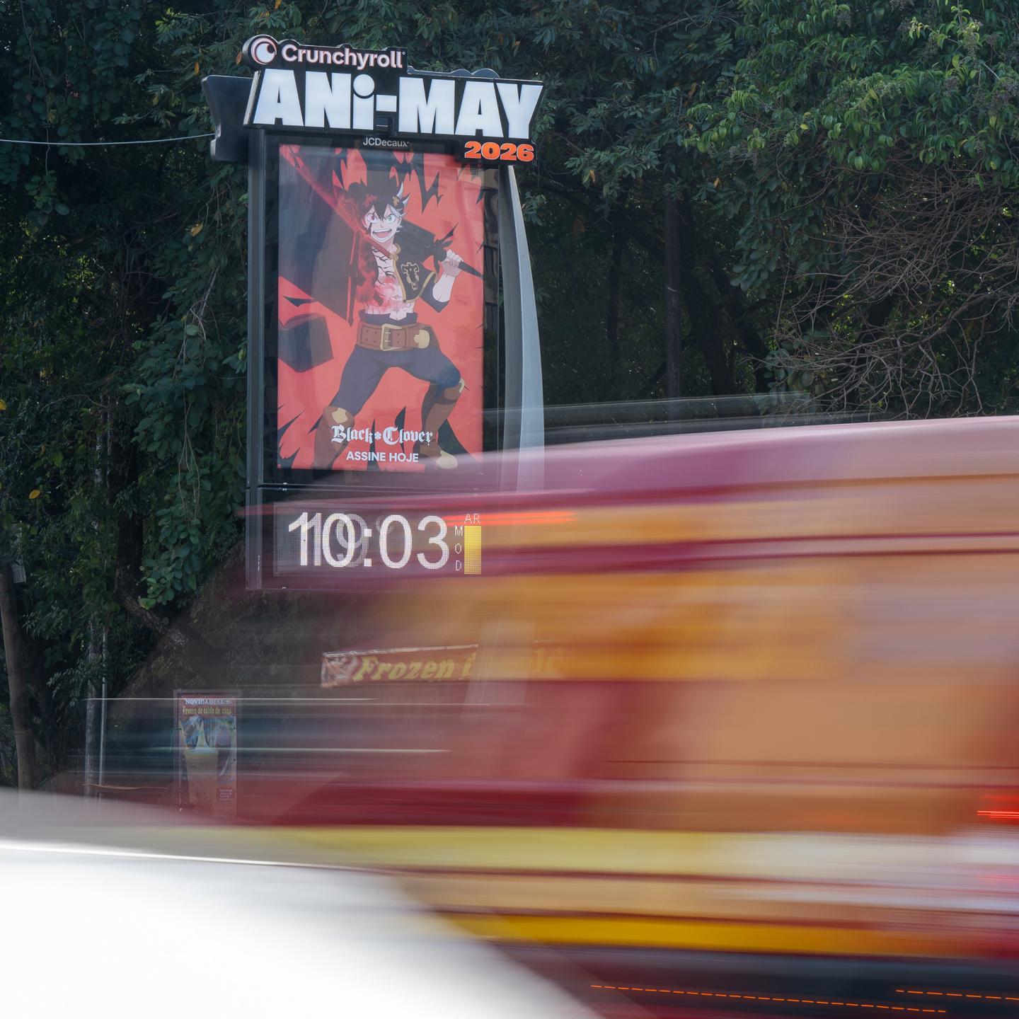 Wide shot of a JCDecaux anime campaign on São Paulo streets, with large Crunchyroll posters on street furniture.