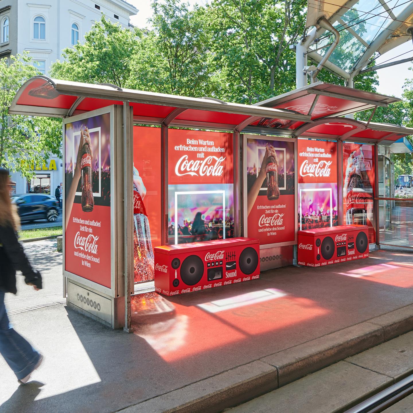 Interior of the Gewista bus shelter showing the red Coca‑Cola ceiling and Eurovision concert posters