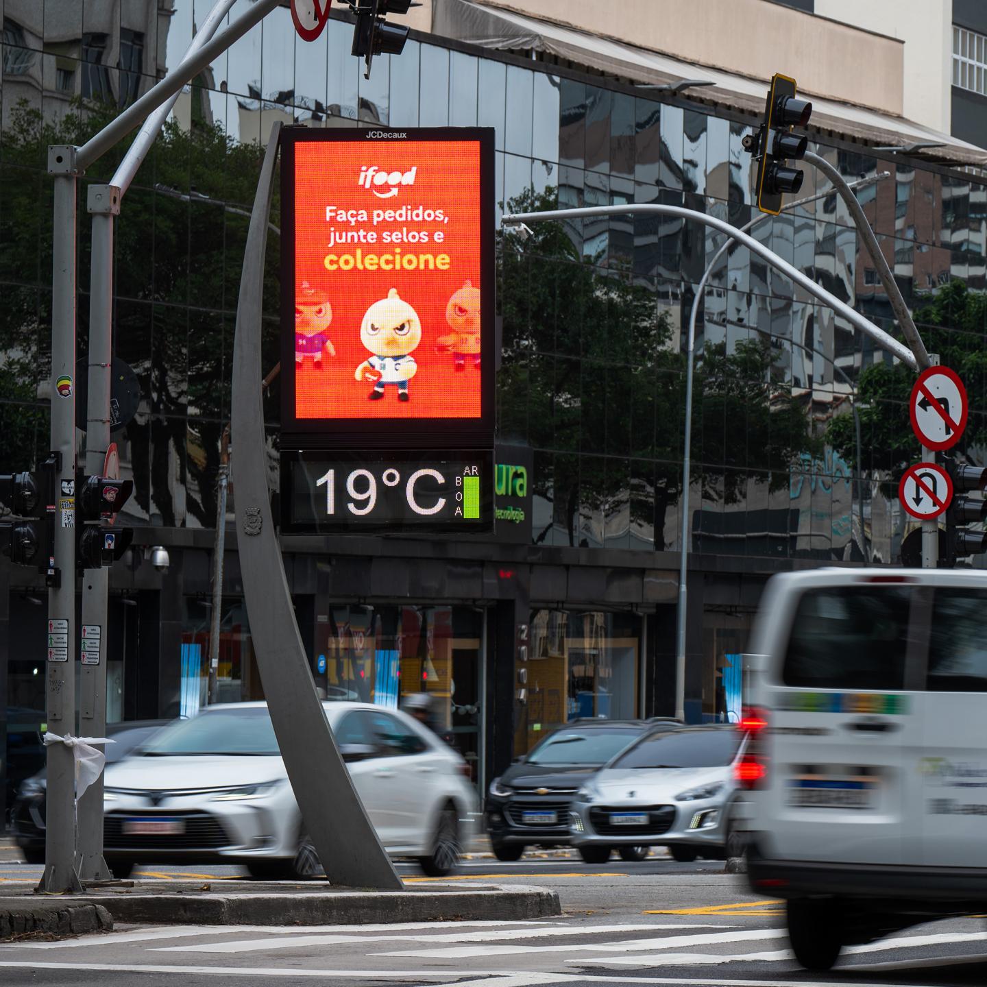 JCDecaux Digital Out-of-Home screen in São Paulo featuring an iFood Canaries character on a red background, with urban traffic and moving cars in the foreground.