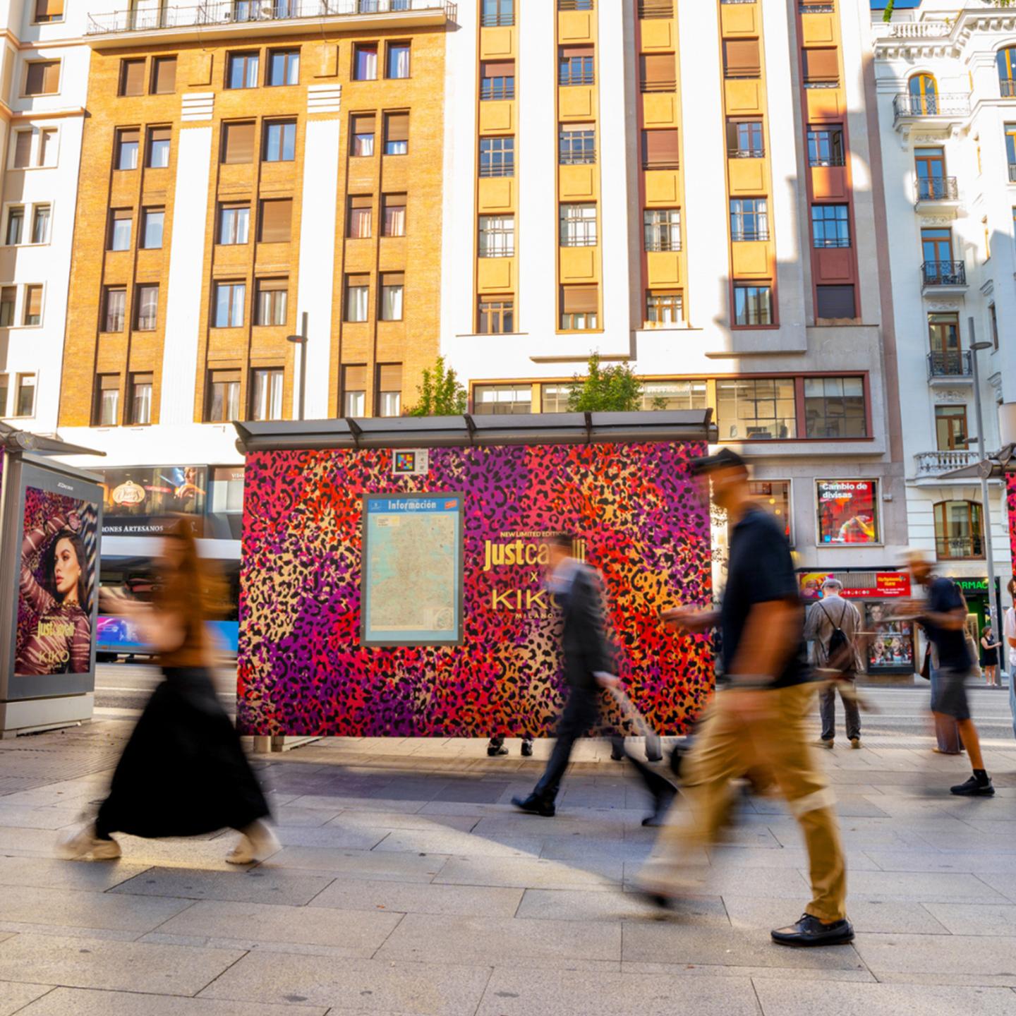 People walking past bright leopard façades of the Just Cavalli x KIKO Milano campaign in Madrid.