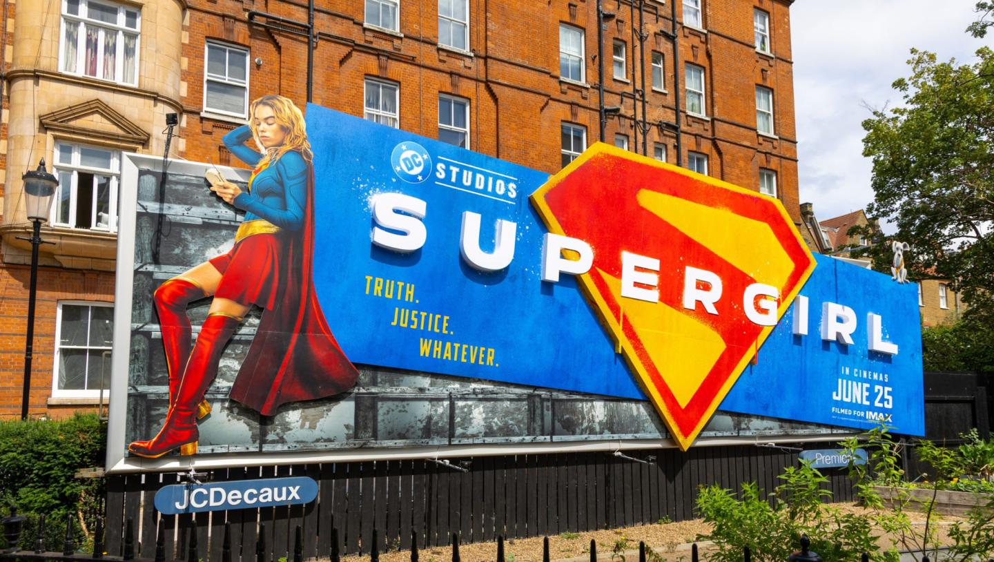 Promotional Supergirl billboard for the DC Studios film, installed on a classic London façade with bold typography and a red‑and‑yellow emblem.