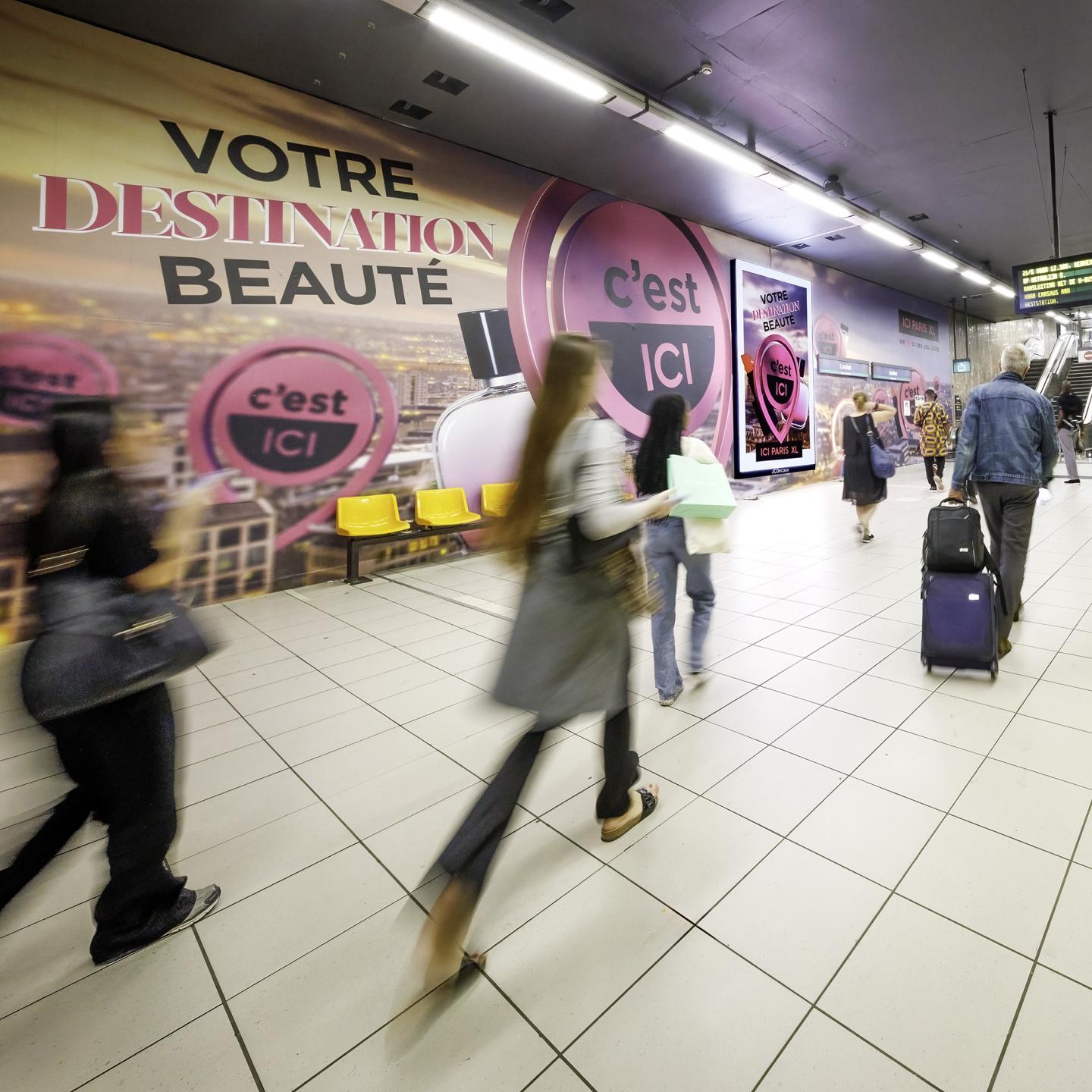 Wide view of JCDecaux ICONIC digital screen and large ICI PARIS XL visuals at Louise station, showing travellers passing through an immersive branded environment.