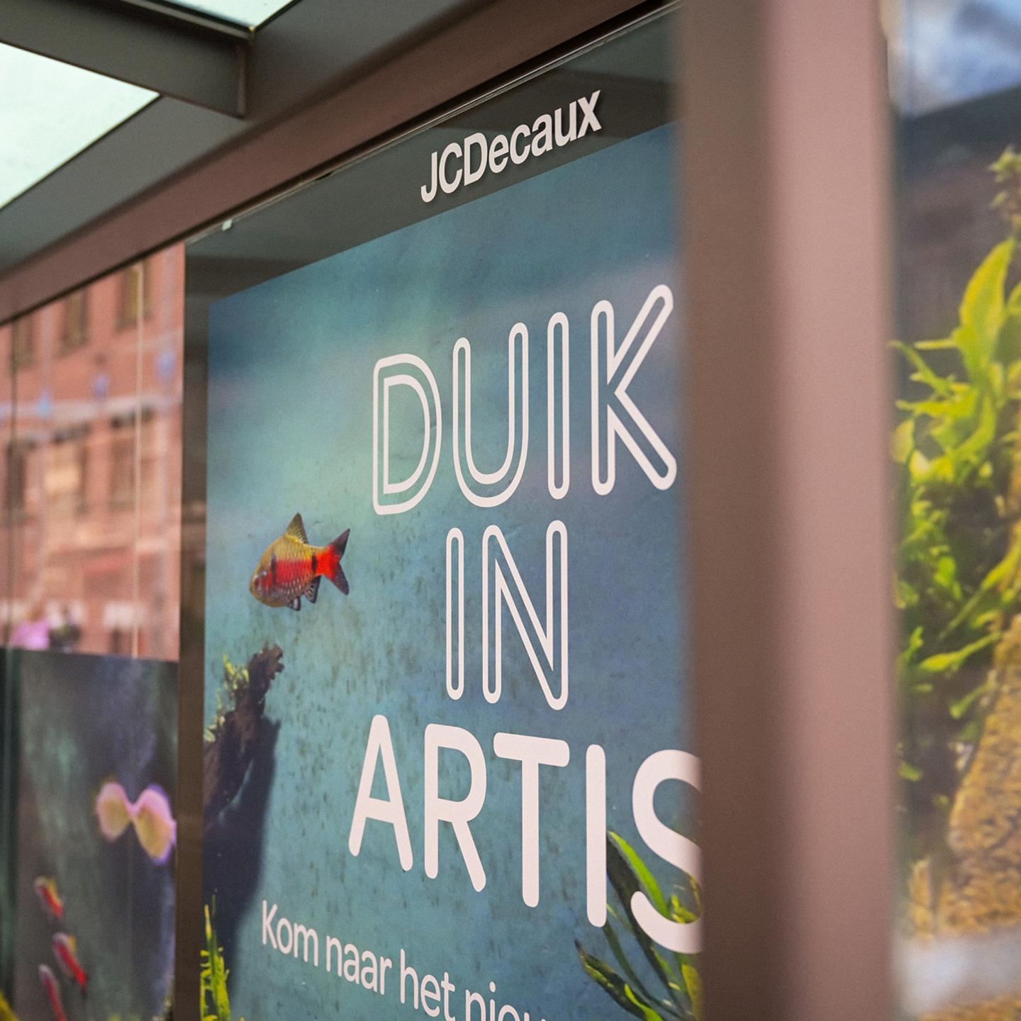 Wide view of a tram and JCDecaux bus shelter with matching marine visuals, guiding pedestrians towards the newly restored Artis aquarium in Amsterdam.