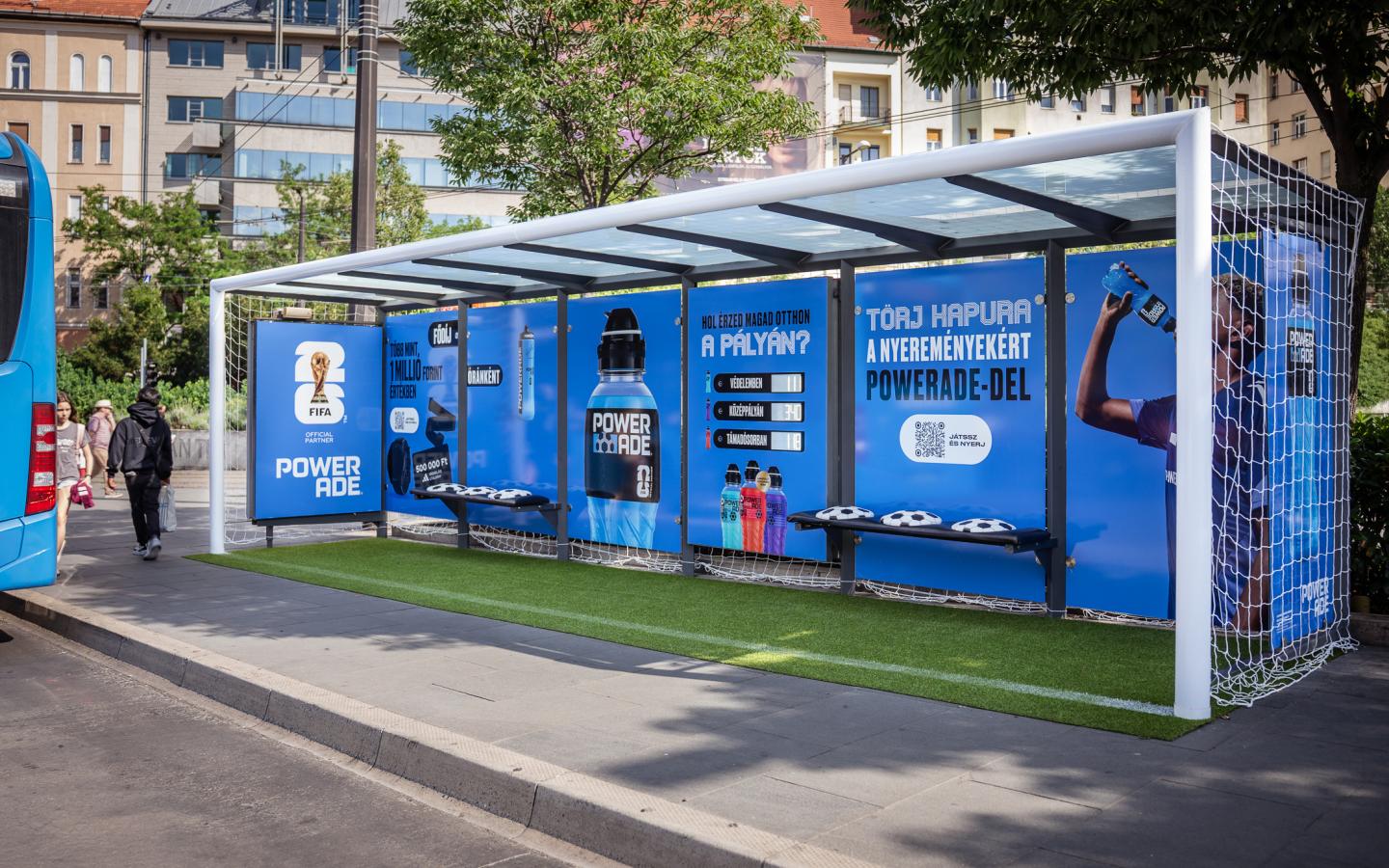 Wide shot of the JCDecaux Powerade installation, where the entire bus shelter is enclosed by goal nets and converted into an open‑air football stadium.