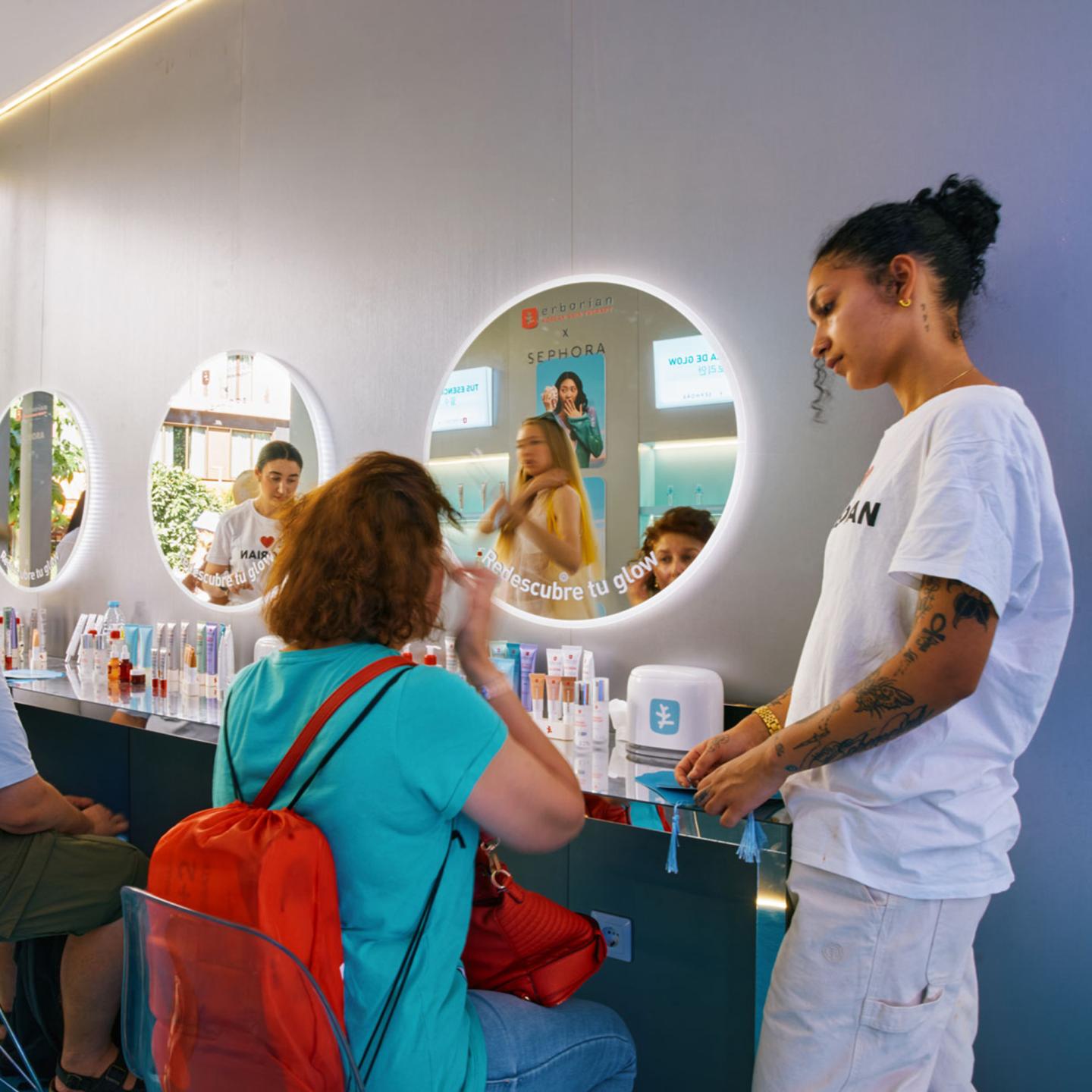 Visitors sitting in front of round mirrors while an Erborian beauty expert offers skincare advice and product testing inside the JCDecaux pop-up in Madrid.