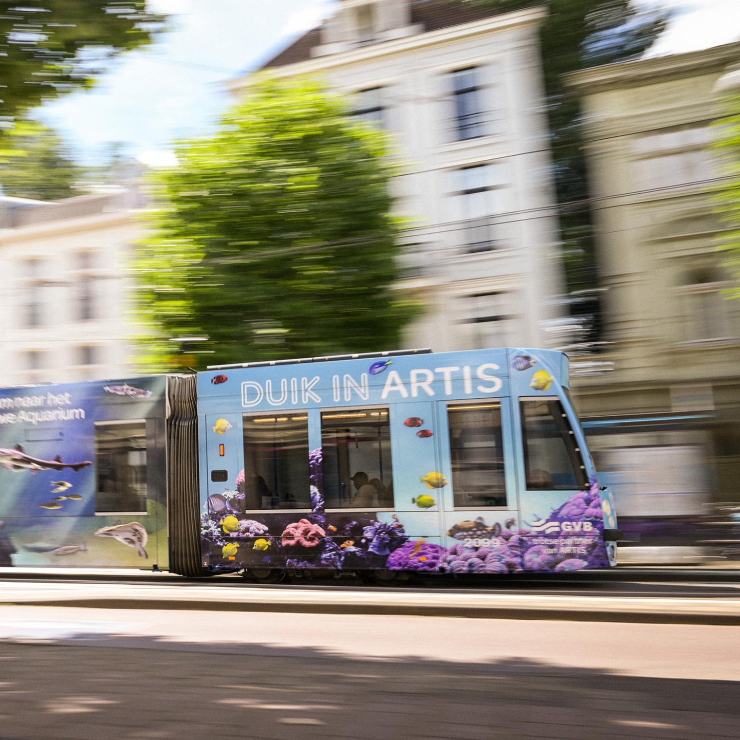 Blue tram wrapped by JCDecaux in Artis aquarium visuals, showing fish and coral reefs as it travels through the streets of Amsterdam.