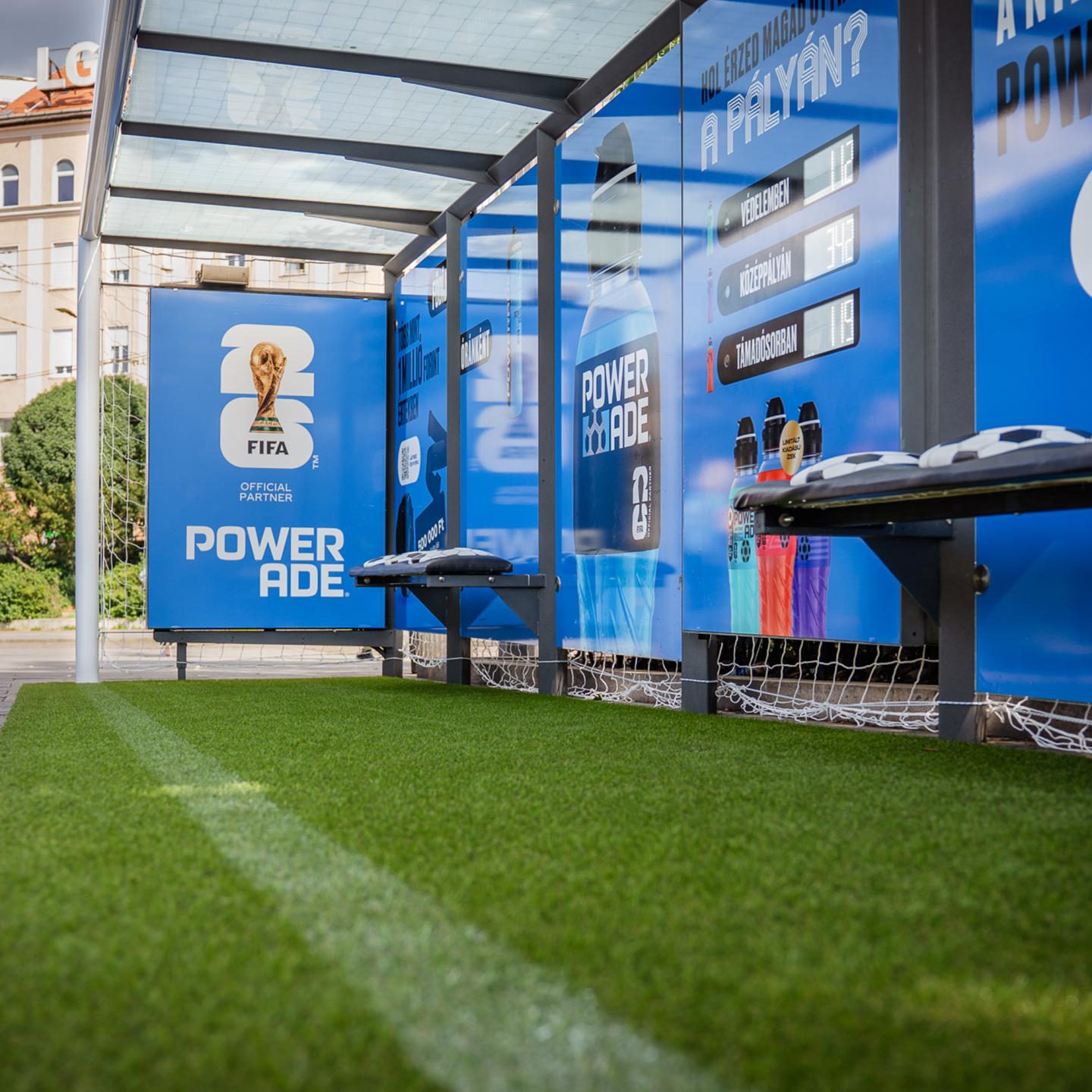 Close‑up of the JCDecaux Powerade bus shelter showing blue World Cup visuals, product bottles and an interactive voting panel for passengers.