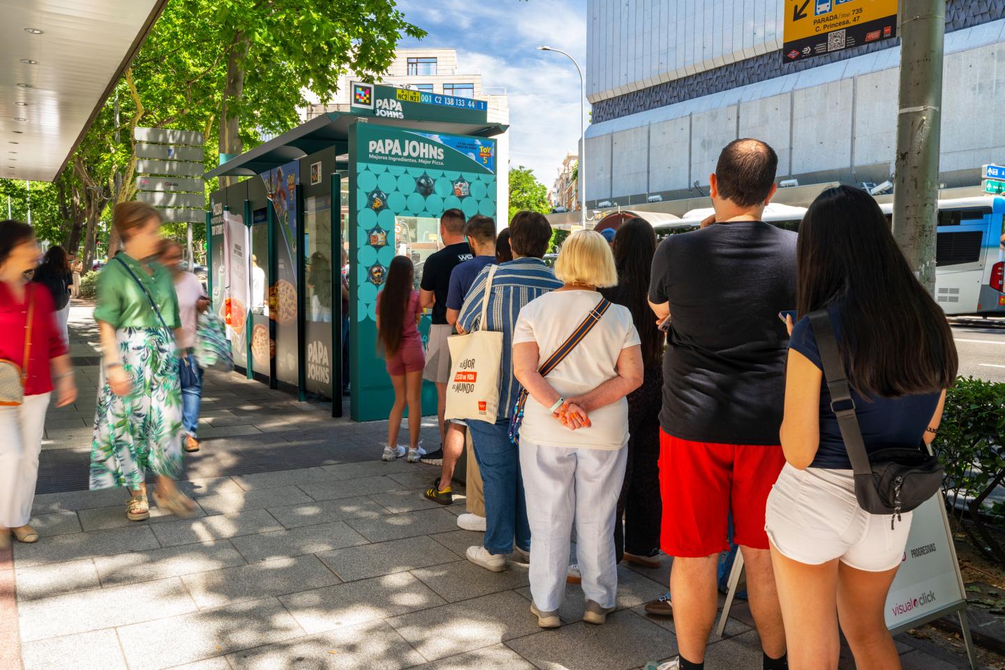 People queuing in front of a JCDecaux bus shelter in Madrid to play the Toy Story 5 claw machine and win Papa Johns pizzas, figurines and discount vouchers.