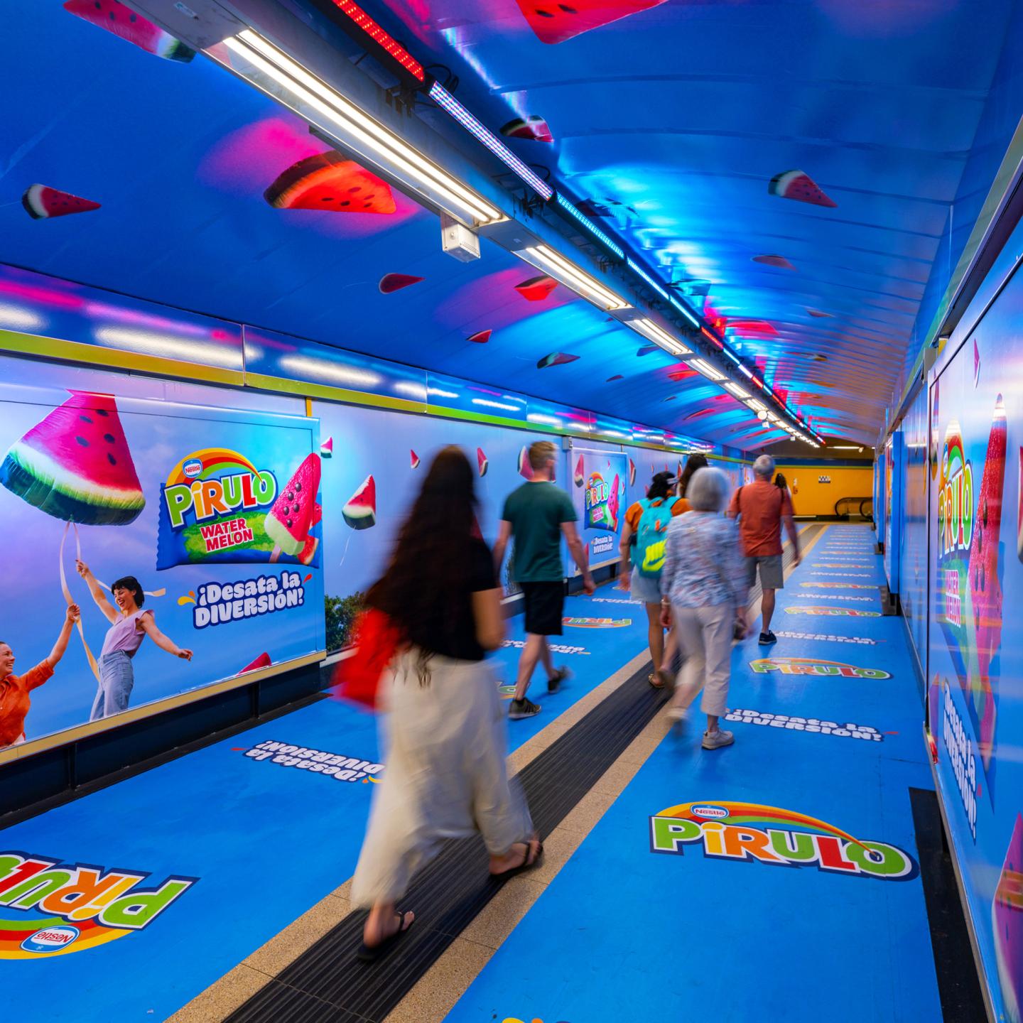 Passengers walking through Callao Metro station redesigned by JCDecaux Spain with vibrant Pirulo Watermelon branding and summer lighting.