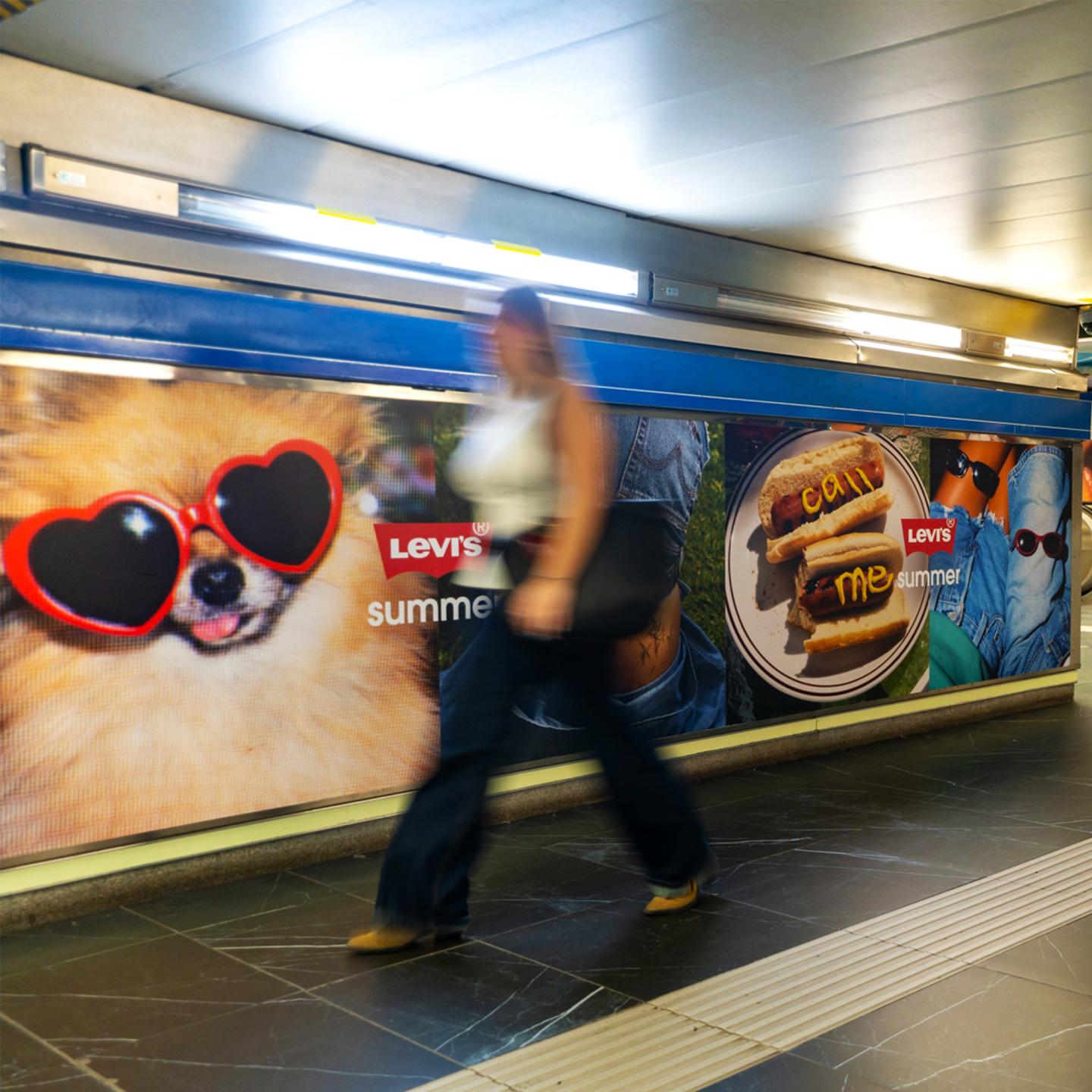 Passengers walking through a brightly branded metro corridor with Levi’s denim, lifestyle visuals and JCDecaux out‑of‑home media formats.