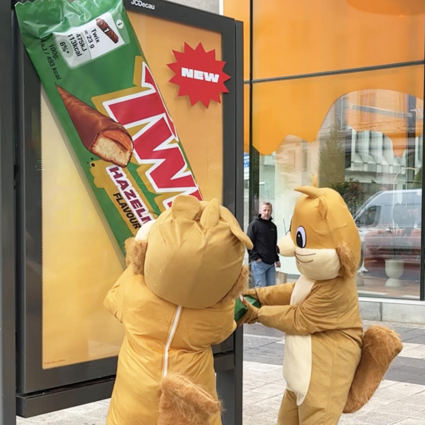Two squirrel mascots from the JCDecaux campaign appearing to steal a giant Twix Hazelnut bar from an outdoor billboard in central Stockholm.