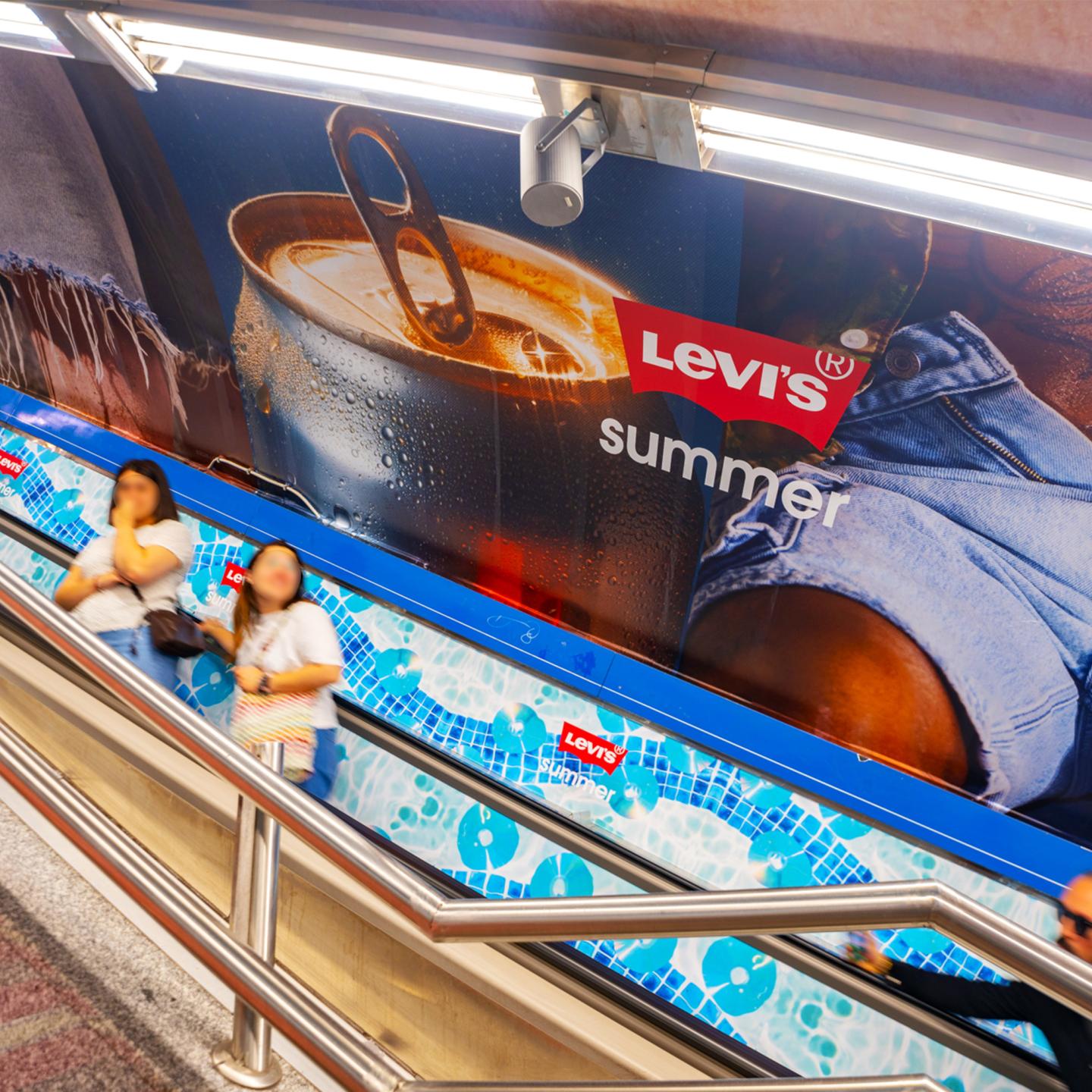 Wide view of Madrid’s Tribunal metro corridors fully wrapped in Levi’s summer imagery, illustrating JCDecaux’s large‑scale station domination.