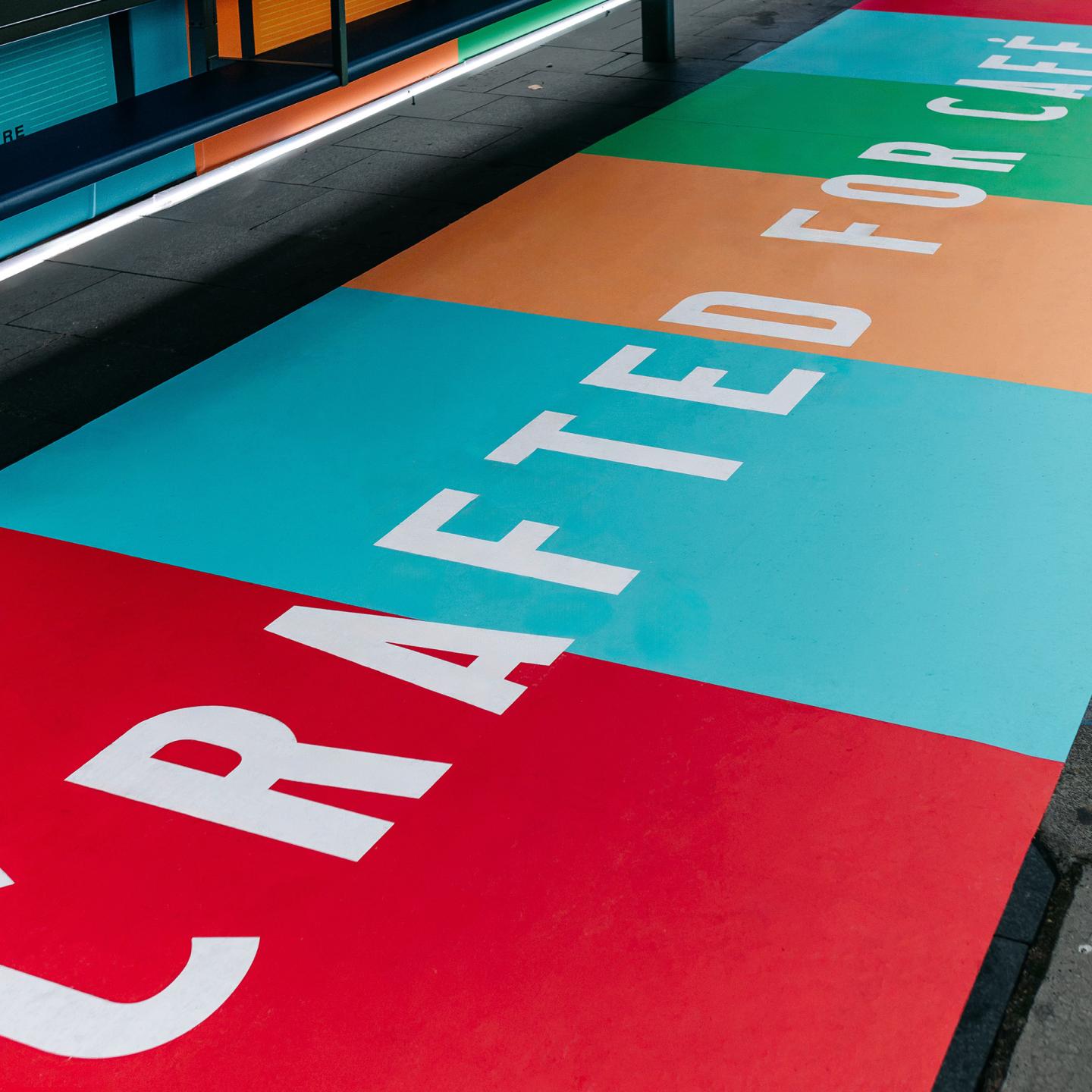 Custom floor decal in front of a JCDecaux bus shelter prompting commuters to choose barista plant-based milk for their morning coffee.