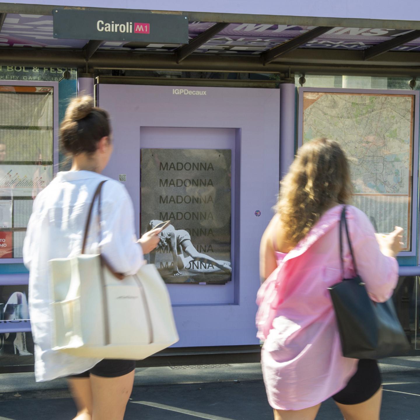 Commuters collecting a free exclusive Madonna poster directly from a custom-built dispenser inside an IGPDecaux bus shelter.