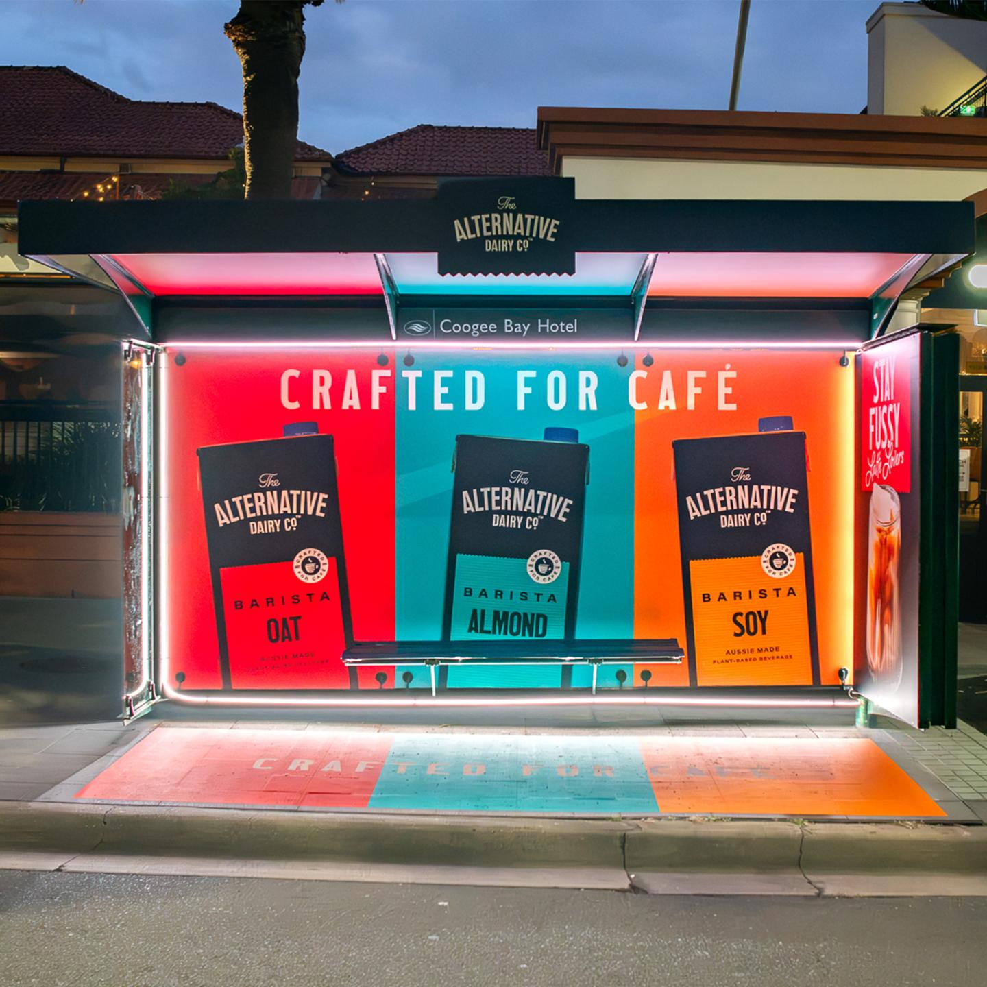 Bus shelter lit up at night with a bright neon sign highlighting a plant-based milk advert in Sydney.