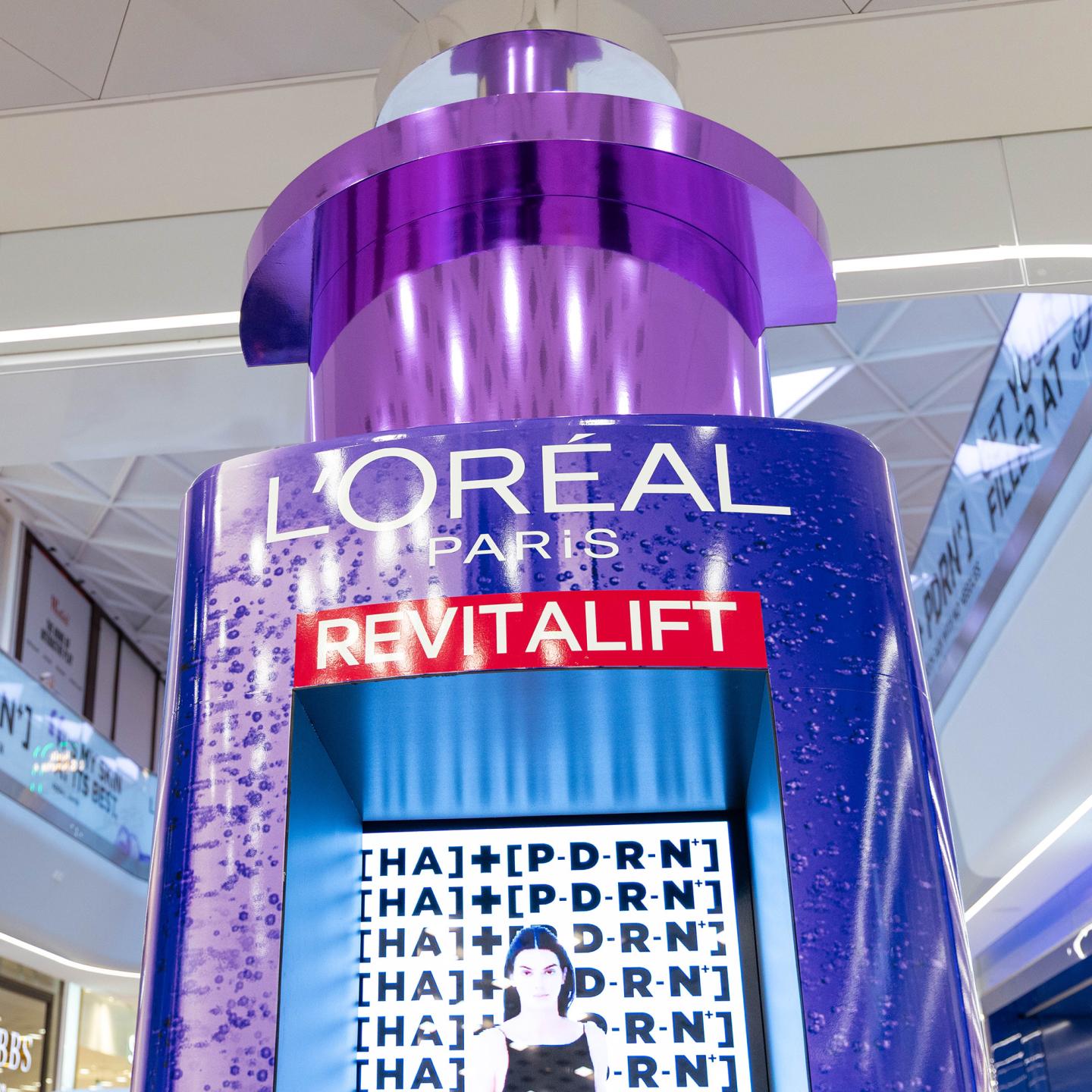 Close-up view of the tall purple 3D L’Oréal Revitalift serum bottle display at Westfield London, highlighting the product branding and digital screen built into the structure.