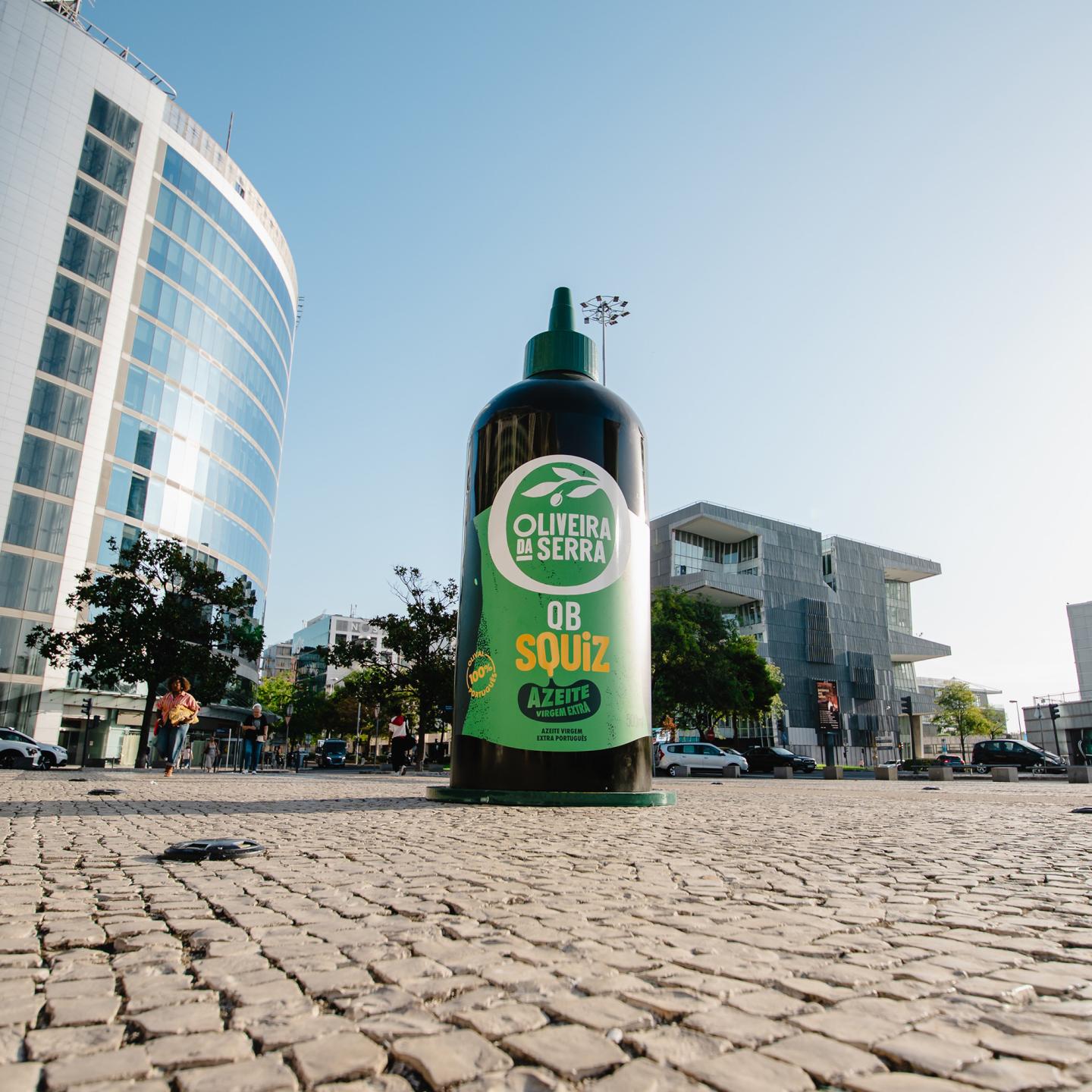 Large green Oliveira da Serra Squiz bottle positioned in the city centre of Lisbon, surrounded by pedestrians and modern architecture as part of a creative out-of-home campaign.