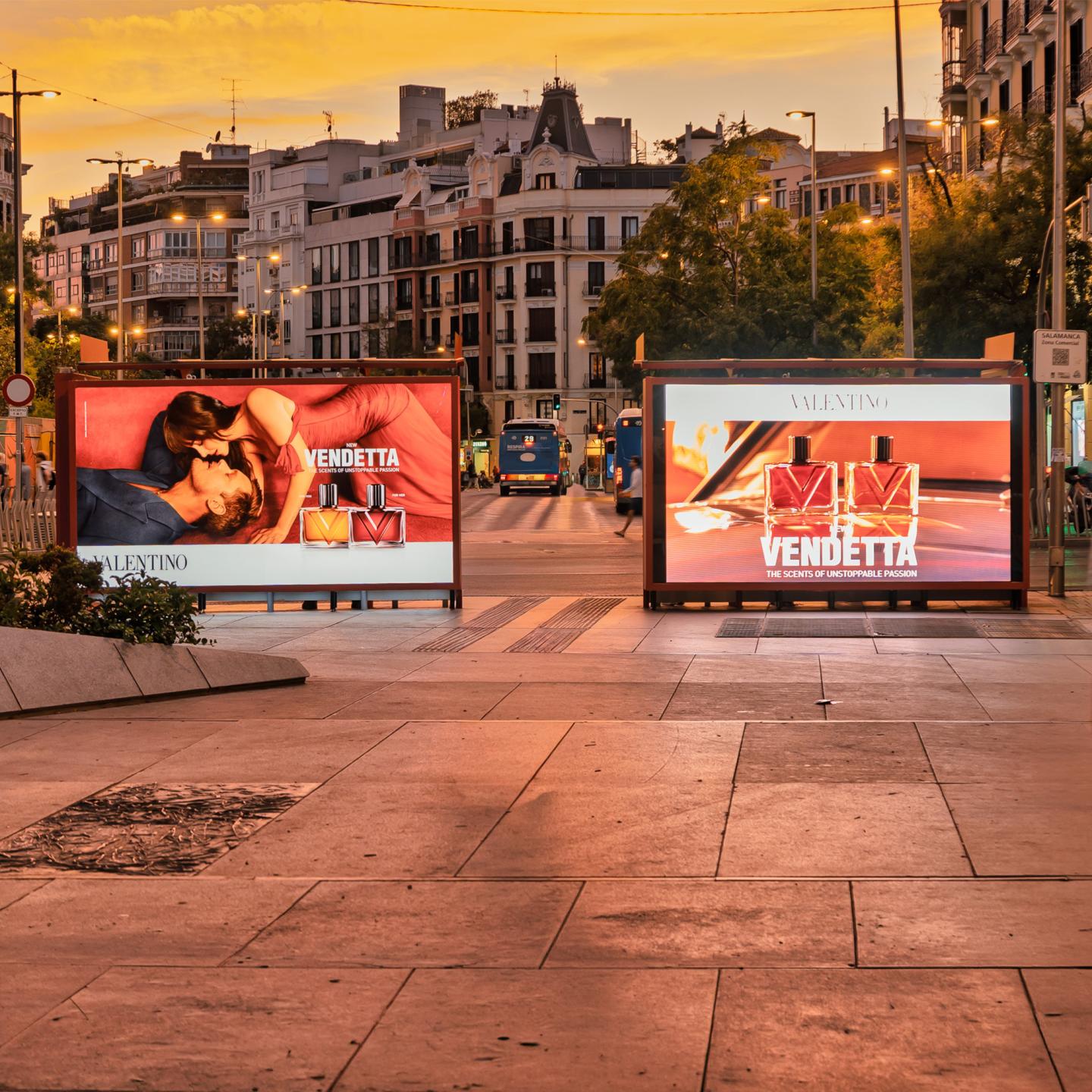 Two illuminated JCDecaux Spain large format panels in a Madrid square at sunset, one showing Valentino Vendetta perfume bottles and the other a romantic campaign visual.