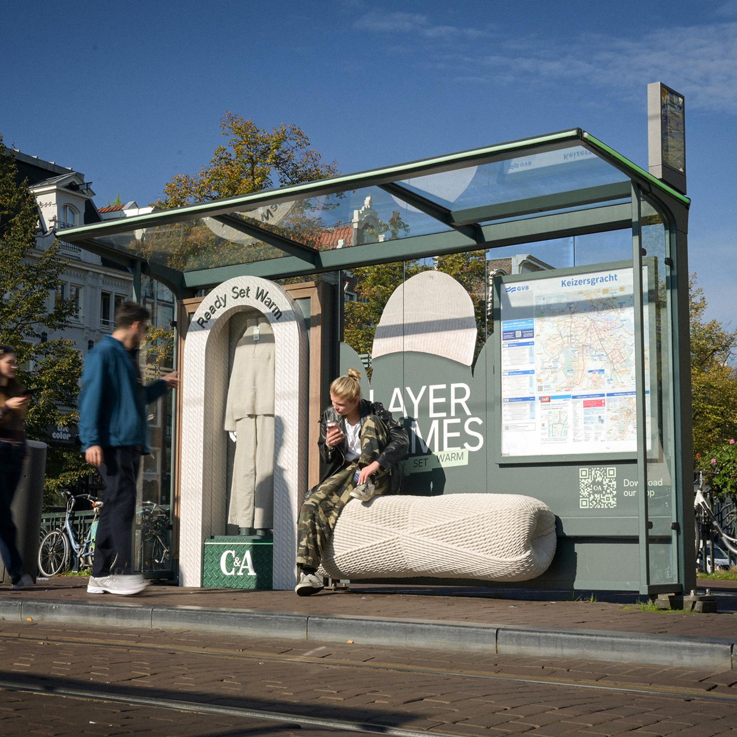 An Amsterdam bus shelter showcasing C&A’s knitwear collection, with a knitted display, textured bench and people waiting nearby.