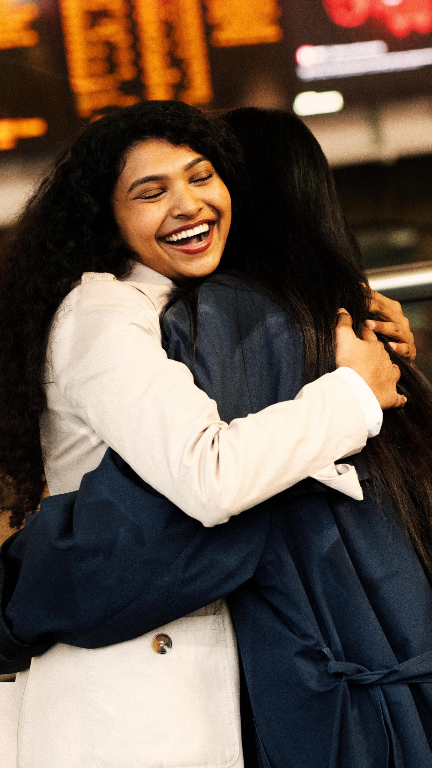 woman hugging someone in front of train station advertising