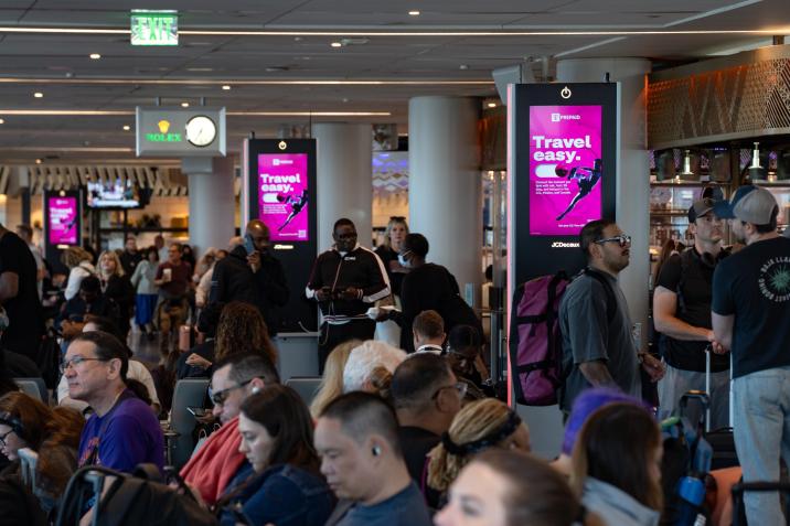 Travelers sit and walk in gatehold area in LAX near three digital T-Mobile OOH ads