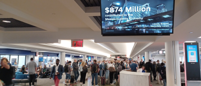 In foreground, digital screen showcases Coca Cola advertising. Mass of people wait to board flight in BOS in background.