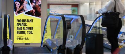 Passengers head down an escalator past a large digital advertisement for Bumble in LAX