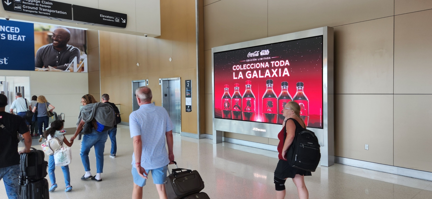 Large screen in HOU shows coca cola star wars partnership as passengers walk by