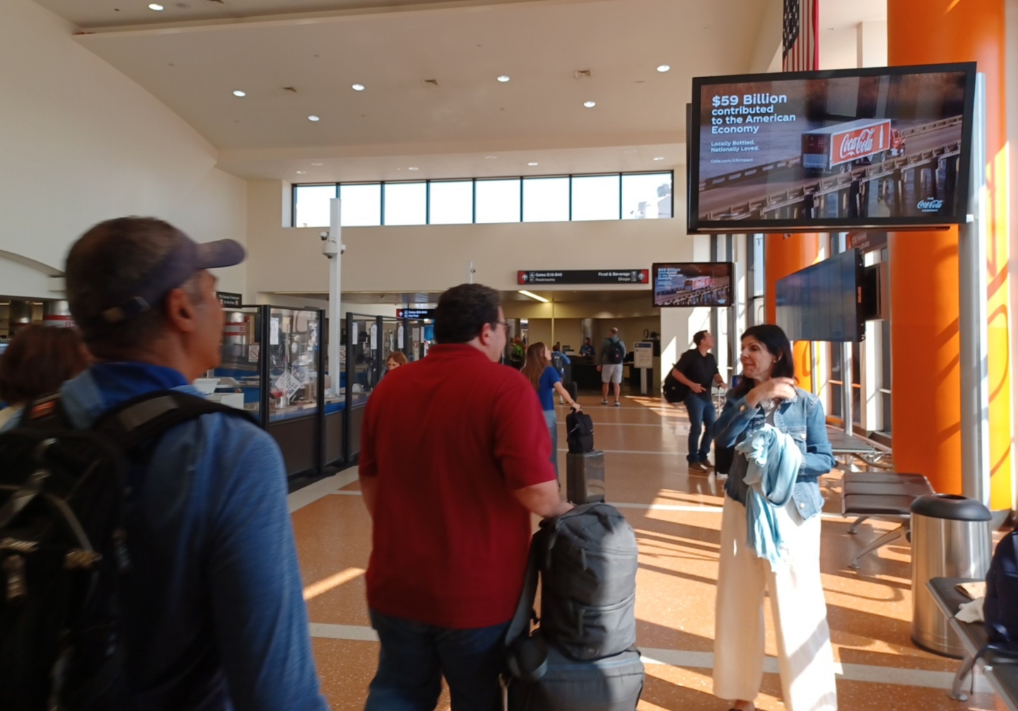 Passengers walk past TSA area and JCDecaux advertising screens with Coca Cola ads