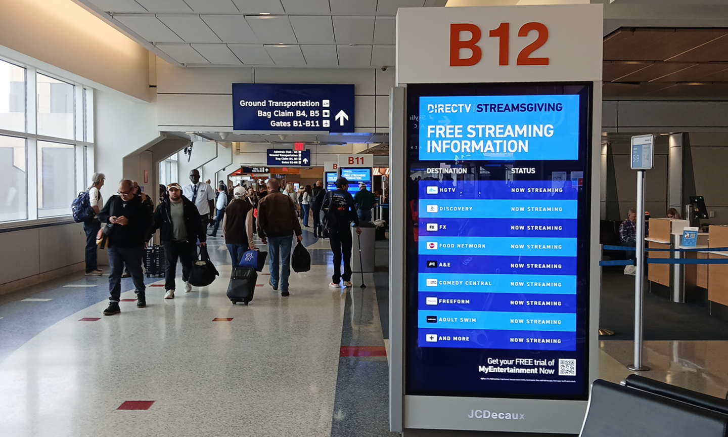Passengers walk past synched digital screens with DirecTV advertising on their way to their gates in DFW