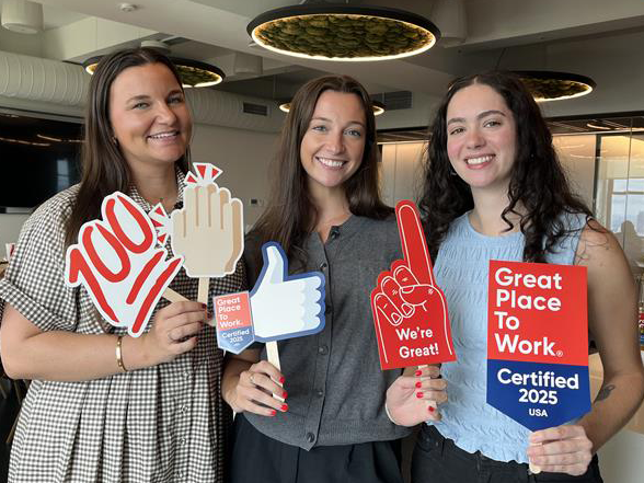 Three female employees hold up signs in recognition of 2025 Great Place to Work certification
