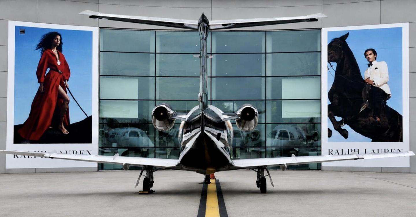 Private jet sits on tarmac in front of large format banners with Ralph Lauren advertising